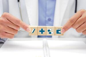 Hand of doctor holding a wooden block cube with healthcare medical icon symbol and below, there is a blurred book placed. Medical and health concept. photo