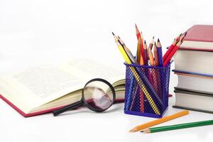 Focus crayon or colored pencils in box and magnifying glass, Blurred books lined up on white background. Learning, study and presentation concept. photo