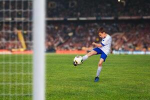 Young soccer player kicks the ball with determination, scoring a goal in a packed stadium under the bright lights of a thrilling match photo