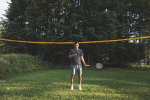 Addicted to the mobile phone even when playing badminton. A black-haired man holding a phone and playing sport. Modern combination of sport and technology. Problem of teenagers today photo