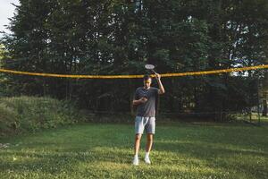 Addicted to the mobile phone even when playing badminton. A black-haired man holding a phone and playing sport. Modern combination of sport and technology. Problem of teenagers today photo