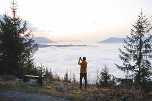 Adventurer takes photos on his mobile phone to capture the sunset and the clouds below. Capturing memories with technology. Beskydy mountains, Czech Republic