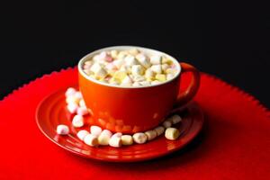 Cocoa drink with colorful small marshmallows on red background photo