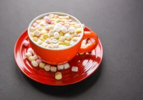 Cocoa drink with colorful small marshmallows on red background photo