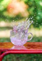 Splash of cool fresh water with ice cube in transparent glass cup in the table outoors in summer day. photo
