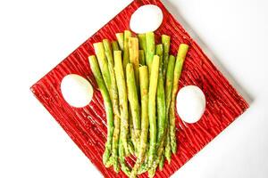 Green grilled asparagus and baked eggs on a red plate photo