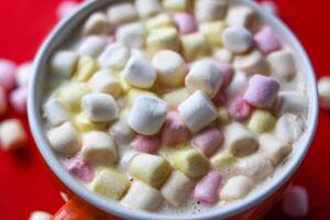 Cocoa drink with colorful small marshmallows on red background photo