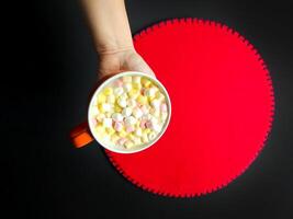 Cocoa drink with colorful small marshmallows on red background photo