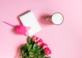 The cup of hot coffee, empty notepad with funny pen and bouquet of fresh roses on soft pink background. photo