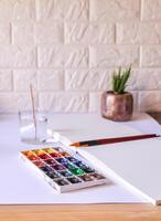 Watercolor paints, brushes, water in glass and paper on white background. Flat lay, top view photo