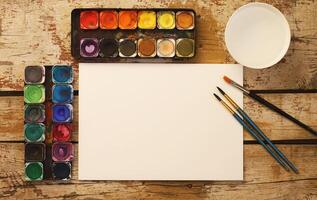 Paper, watercolors, paint brush and some art stuff on wooden table photo