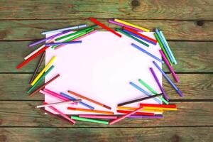 School supplies. Back to School design elements. Colorful markers and white empty paper sheet on aged wooden table background. photo