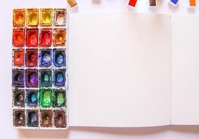 Watercolor paints, brushes and paper on white background. Flat lay, top view photo