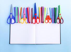 School supplies. Back to School design elements. Colorful markers and scissors on opened empty notepad on light blue paper background. photo