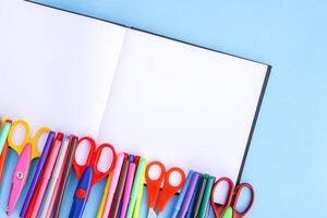 School supplies. Back to School design elements. Colorful markers and scissors on opened empty notepad on light blue paper background. photo