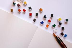 Watercolor paints, brushes and paper on white background. Flat lay, top view photo