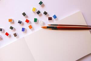 Watercolor paints, brushes and paper on white background. Flat lay, top view photo