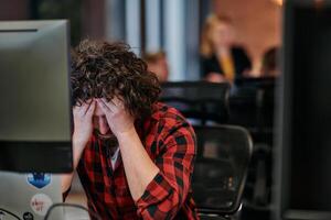 Disappointed Programmer with Messy Hair Looking at Computer Monitor in Office. photo