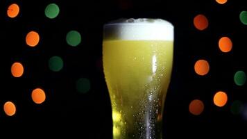 A glass of cold light foamy beer stands on a table on a black background with colored lights. Beer is foaming in a glass. video