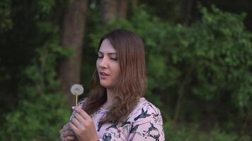attractive girl blowing dandelion in the forest in summer in sunny weather. slow motion video