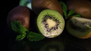 Fruits of juicy kiwi and mint leaves rotate on a table on a black background. Close-up video