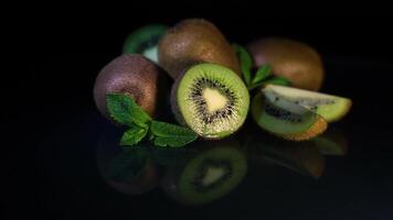 Fruits of juicy kiwi and mint leaves rotate on a table on a black background. HD video