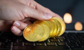 Close up of human hand put some pieces of golden Bitcoin token on laptop. Bitcoin is one of the popular cryptocurrency, a virtual currency or a digital currency. photo