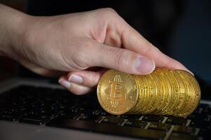 Close up of human hand put some pieces of golden Bitcoin token on laptop. Bitcoin is one of the popular cryptocurrency, a virtual currency or a digital currency. photo
