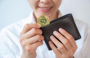 Happiness woman holding leather wallet with a golden Bitcoin token in her hands. Bitcoin is one of the popular cryptocurrency, a virtual currency or a digital currency. photo