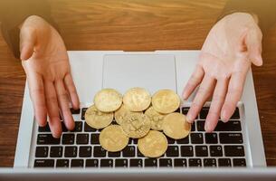Close up of human hand put some pieces of golden Bitcoin token on laptop. Bitcoin is one of the popular cryptocurrency, a virtual currency or a digital currency. photo