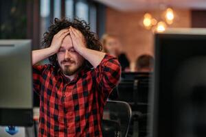 Disappointed Programmer with Messy Hair Looking at Computer Monitor in Office. photo