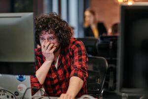 Disappointed Programmer with Messy Hair Looking at Computer Monitor in Office. photo