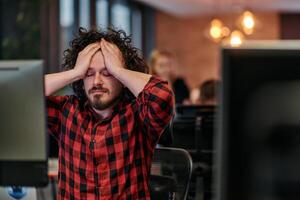 Disappointed Programmer with Messy Hair Looking at Computer Monitor in Office. photo