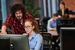 Business colleagues, a man and a woman, engage in discussing business strategies while attentively gazing at a computer monitor, epitomizing collaboration and innovation photo