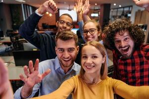 A diverse group of business professionals take a break from their tasks in a modern startup office to capture a creative selfie, showcasing teamwork and a vibrant workplace culture photo