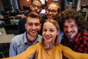 A diverse group of business professionals take a break from their tasks in a modern startup office to capture a creative selfie, showcasing teamwork and a vibrant workplace culture photo