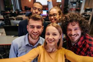 A diverse group of business professionals take a break from their tasks in a modern startup office to capture a creative selfie, showcasing teamwork and a vibrant workplace culture photo