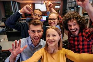 A diverse group of business professionals take a break from their tasks in a modern startup office to capture a creative selfie, showcasing teamwork and a vibrant workplace culture photo
