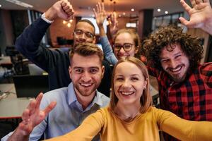 A diverse group of business professionals take a break from their tasks in a modern startup office to capture a creative selfie, showcasing teamwork and a vibrant workplace culture photo