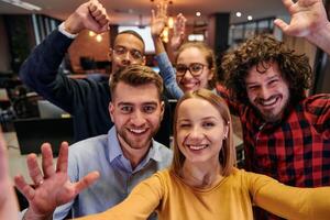 A diverse group of business professionals take a break from their tasks in a modern startup office to capture a creative selfie, showcasing teamwork and a vibrant workplace culture photo
