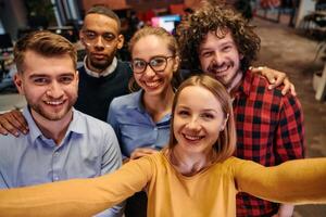 A diverse group of business professionals take a break from their tasks in a modern startup office to capture a creative selfie, showcasing teamwork and a vibrant workplace culture photo