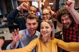 A diverse group of business professionals take a break from their tasks in a modern startup office to capture a creative selfie, showcasing teamwork and a vibrant workplace culture photo