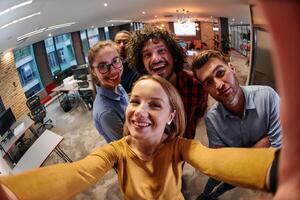 A diverse group of business professionals take a break from their tasks in a modern startup office to capture a creative selfie, showcasing teamwork and a vibrant workplace culture photo