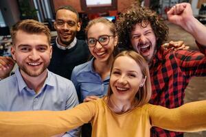A diverse group of business professionals take a break from their tasks in a modern startup office to capture a creative selfie, showcasing teamwork and a vibrant workplace culture photo