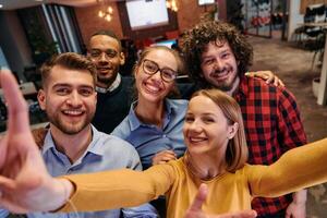 A diverse group of business professionals take a break from their tasks in a modern startup office to capture a creative selfie, showcasing teamwork and a vibrant workplace culture photo
