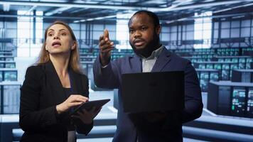 System administrators in data center overseeing server operations using notebook and tablet. Colleagues brainstorming in server hub, ensuring optimal performance and data integrity, camera A video