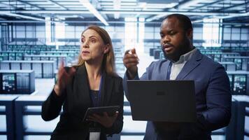 System administrators in data center overseeing server operations using notebook and tablet. Colleagues brainstorming in server hub, ensuring optimal performance and data integrity, camera B video