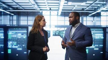 Teamworking technicians in high tech data center workspace looking at hologram visualization. Programmer and colleague working on securing server room hardware using AR tech, camera B video