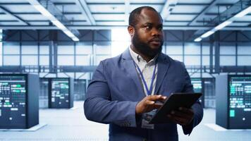 Software developer managing data center with advanced technology, ensuring efficient network management. Admin walking in server room, optimizing data center infrastructure with tablet, camera B video
