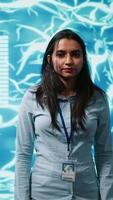 Vertical Portrait of smiling IT specialist standing with arms crossed in front of cutting edge display featuring AI and neural network graphics. Researcher in startup doing advancements in AI field, camera A video